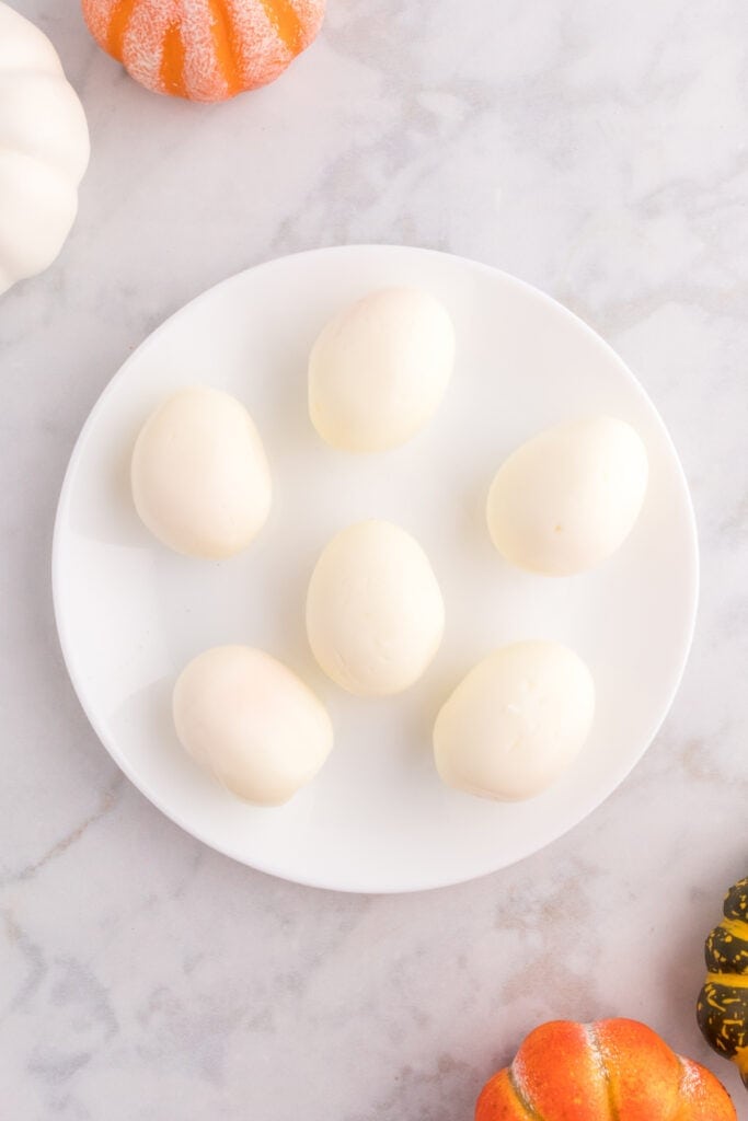 Six peeled hard-boiled eggs on a white plate ready to make Halloween deviled eggs.