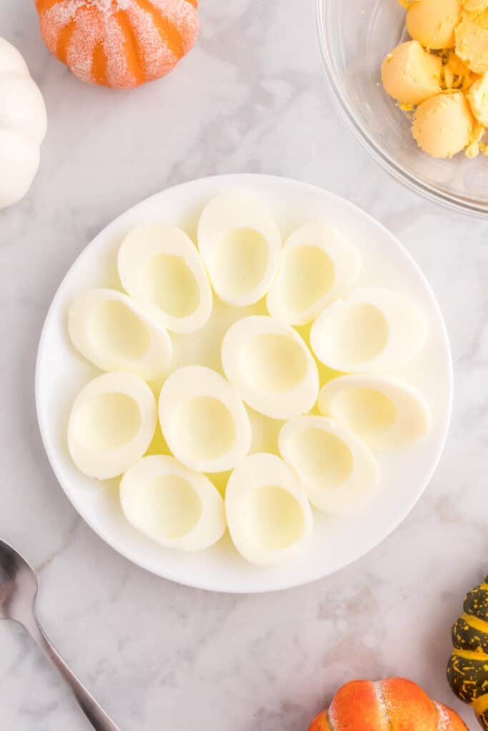 Hard-boiled egg whites arranged on a plate with the cooked yolks removed for deviled egg filling.