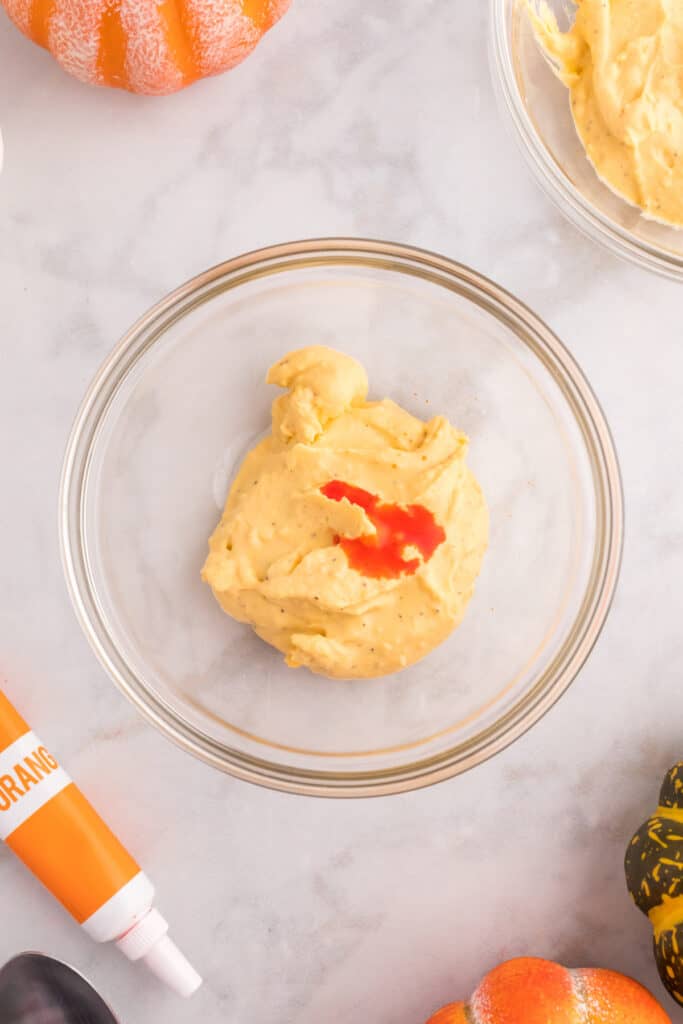 Deviled egg filling in a glass bowl with orange gel food coloring being added for Halloween deviled eggs.