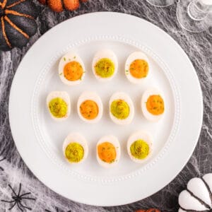 Easy Halloween deviled eggs with orange and neon green filling arranged on a white platter with spooky Halloween decorations.