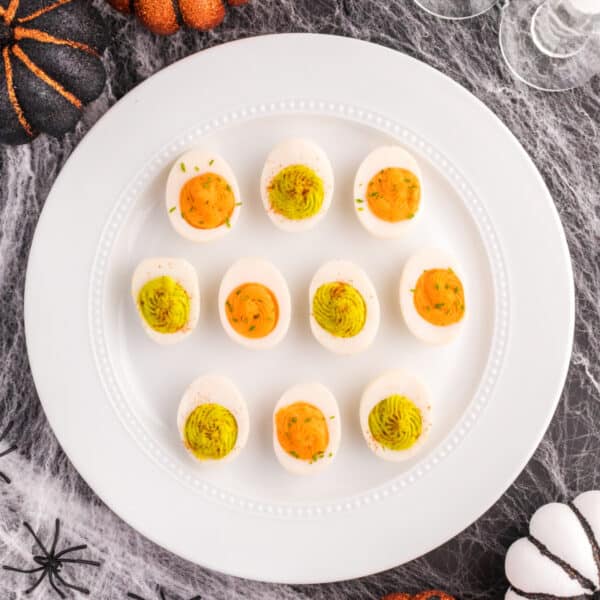 Easy Halloween deviled eggs with orange and neon green filling arranged on a white platter with spooky Halloween decorations.
