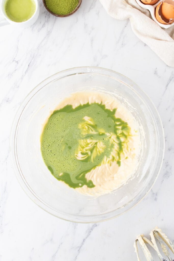 Matcha milk added to the cupcake batter in a glass mixing bowl