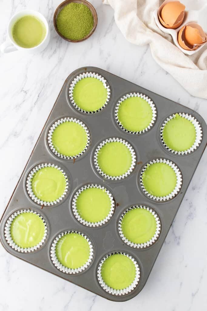 Matcha cupcake batter divided among paper liners in a 12-count cupcake pan