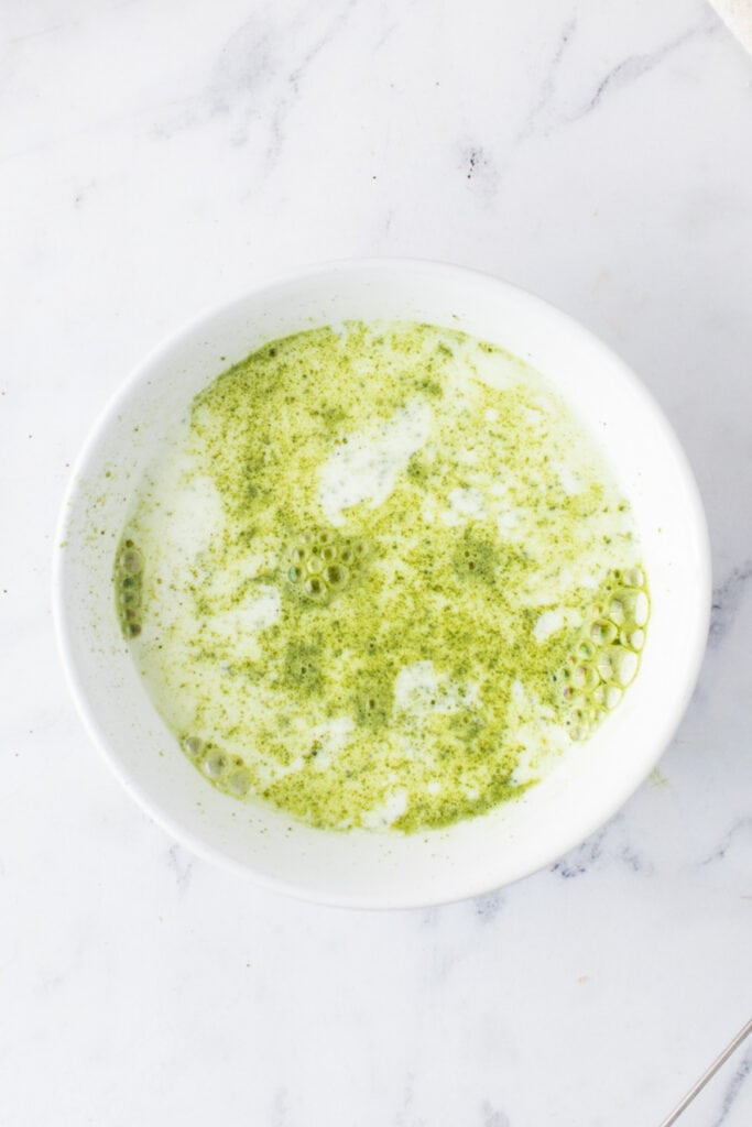 Matcha powder added to warm milk in a white bowl