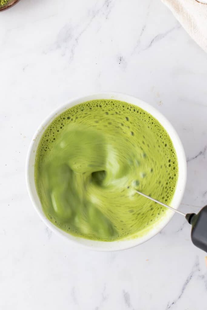 Matcha powder and warm milk being blended with a milk frother