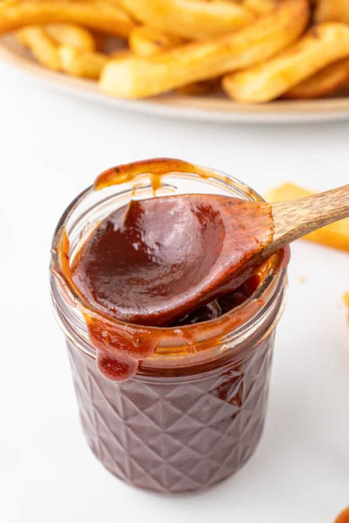 Thick homemade BBQ ranch sauce on a wooden spoon over a glass jar