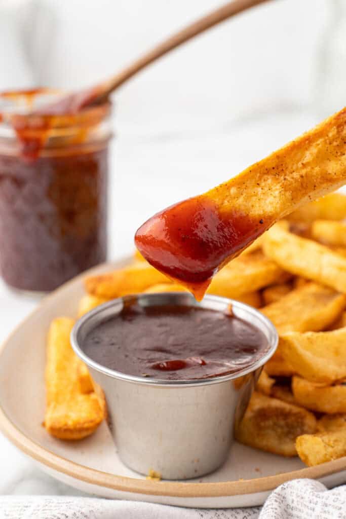 French fry dipped into sweet and spicy OMG Sauce with more fries in the background
