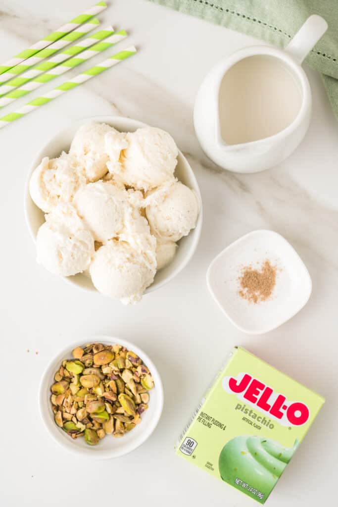 Ingredients for a pistachio milkshake including vanilla ice cream, milk, pistachio pudding mix, cardamom, and chopped pistachios