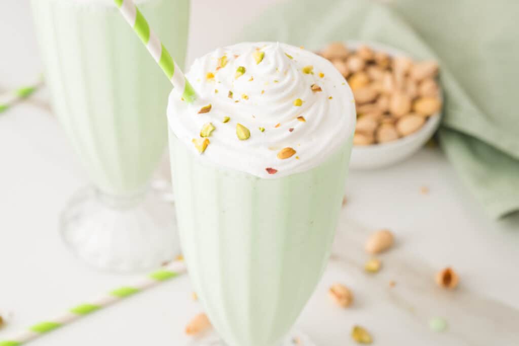 Creamy pistachio milkshake with whipped cream, chopped pistachios, and a striped straw