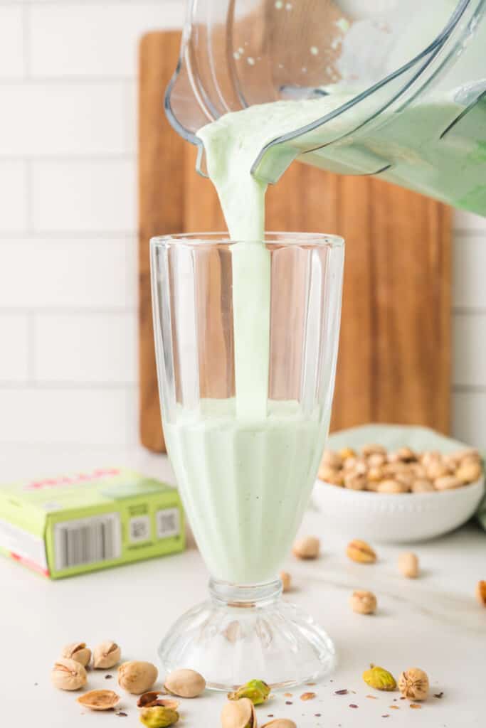 Creamy pistachio milkshake being poured from a blender into a tall glass