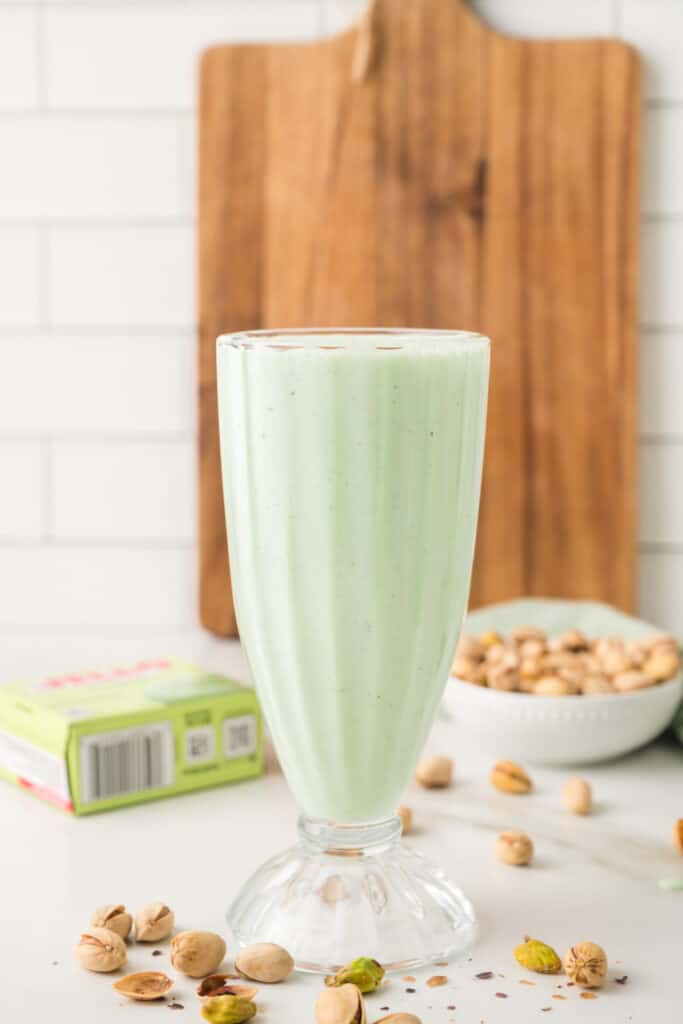Freshly blended pistachio milkshake in a tall glass with pistachios scattered around it