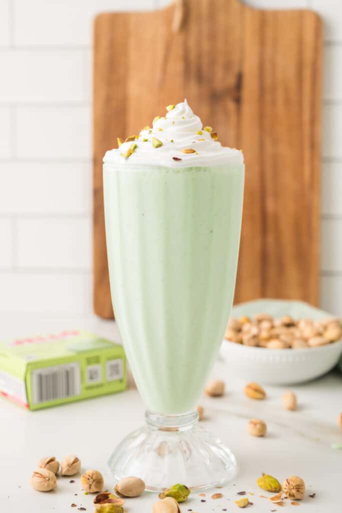 Pistachio milkshake topped with whipped cream and chopped pistachios in a tall glass