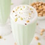 Pistachio milkshake topped with whipped cream and chopped pistachios in a square food photo