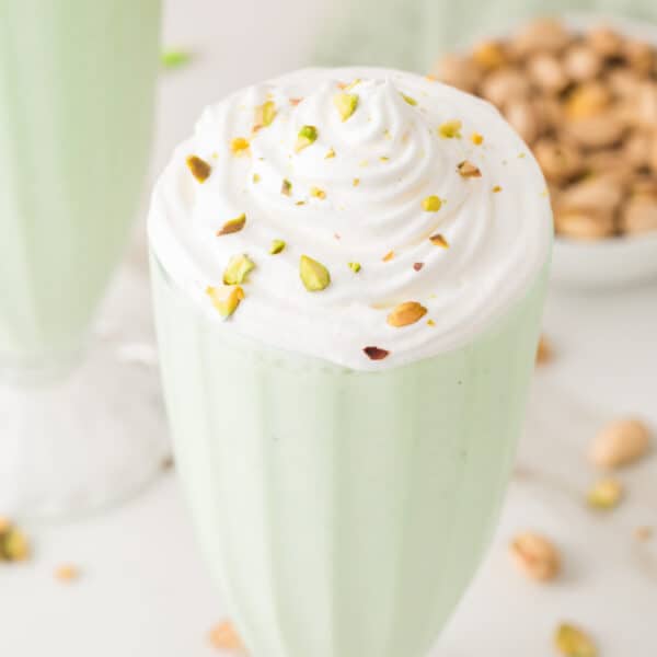 Pistachio milkshake topped with whipped cream and chopped pistachios in a square food photo