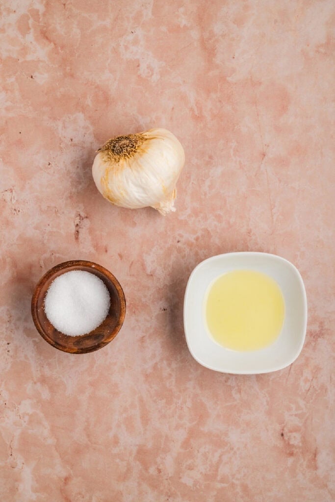 Ingredients for roasted garlic including a whole garlic bulb, olive oil, and salt