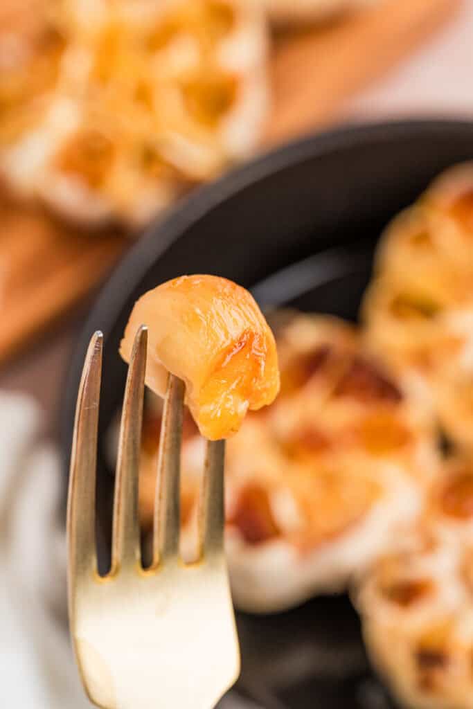 Soft caramelized roasted garlic clove held on a fork