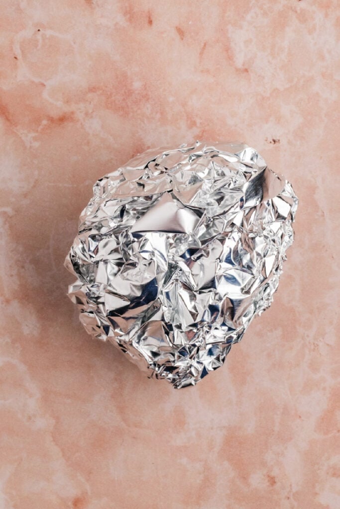 Prepared garlic bulb wrapped tightly in aluminum foil before cooking