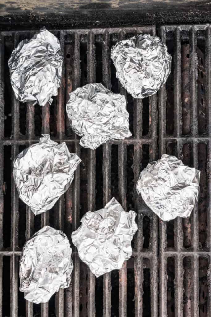 Foil-wrapped garlic bulbs cooking over indirect heat on the grill