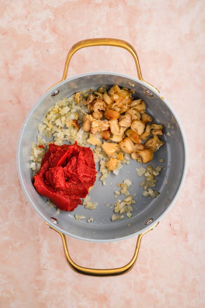 Roasted garlic and tomato paste added to sautéed onions in a saucepan.