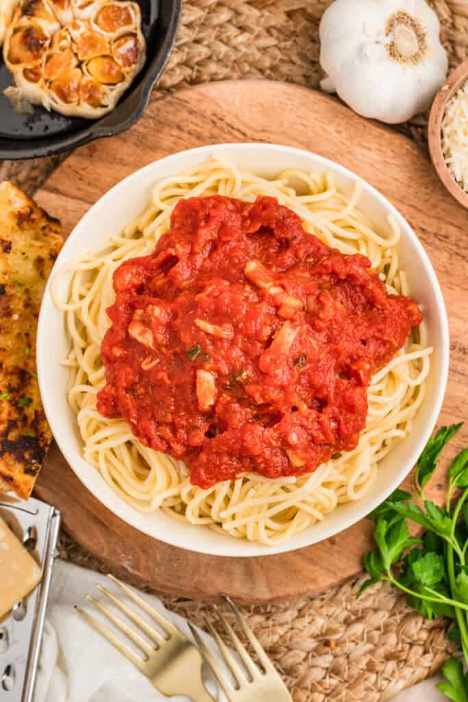 Roasted garlic pasta sauce spooned generously over a bowl of spaghetti with garlic bread on the side.