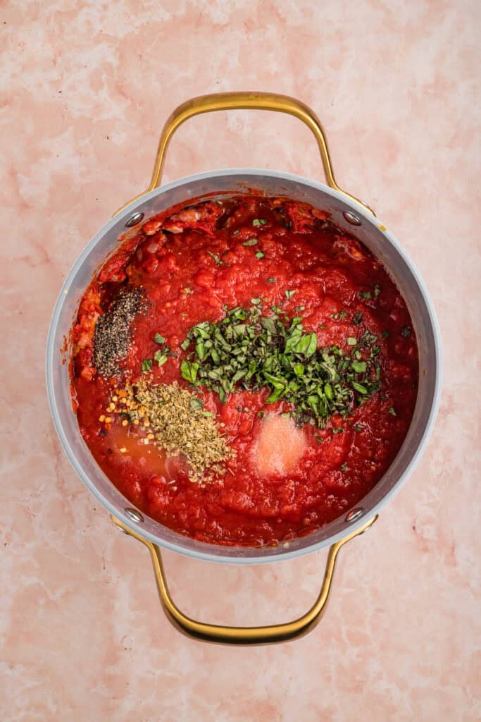 Crushed tomatoes, fresh basil, oregano, seasonings, and red pepper flakes added to the saucepan.