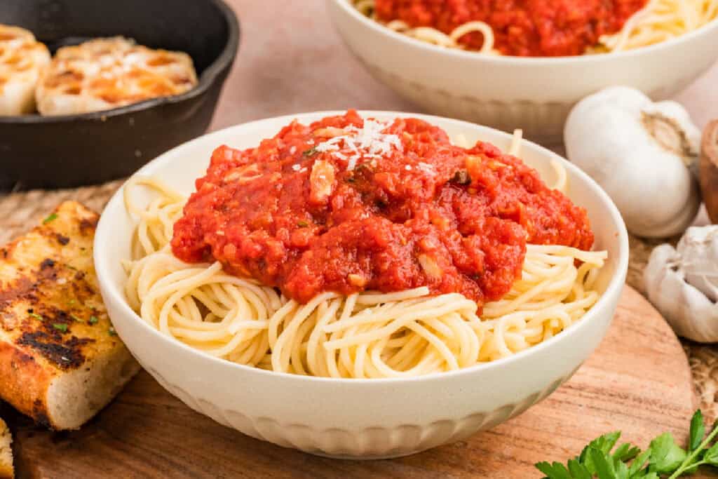 Bowl of spaghetti topped with chunky roasted garlic tomato sauce and Parmesan, served with garlic bread.