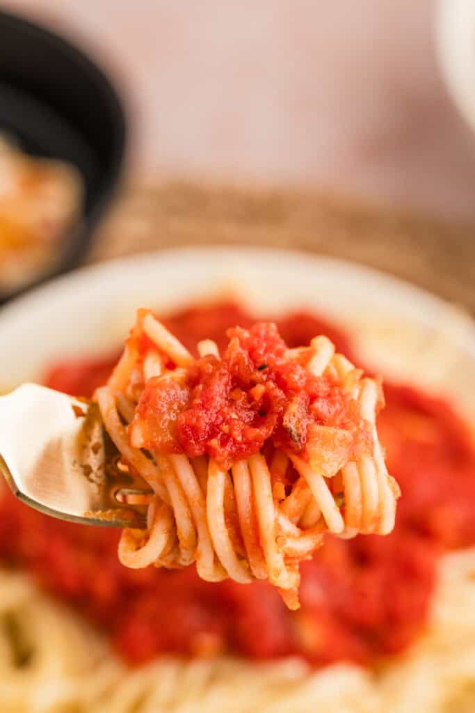 Forkful of spaghetti coated with roasted garlic pasta sauce above a bowl of pasta.