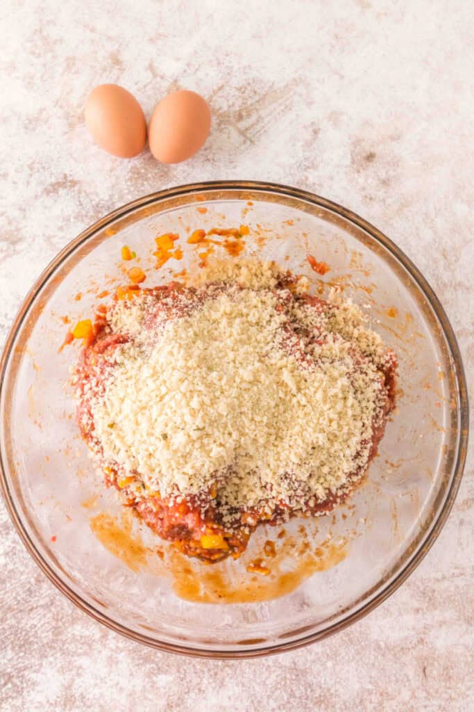 Breadcrumbs added to the cowboy meatloaf mixture with two eggs ready to be mixed in
