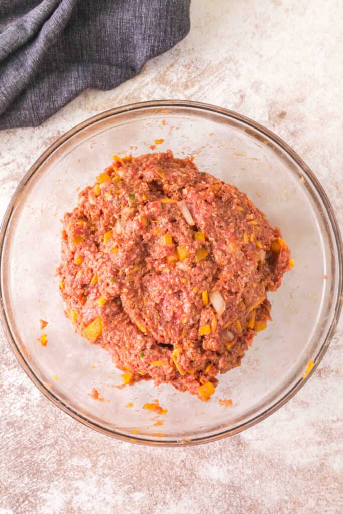 Fully combined raw cowboy meatloaf mixture with chopped peppers and onions in a glass bowl