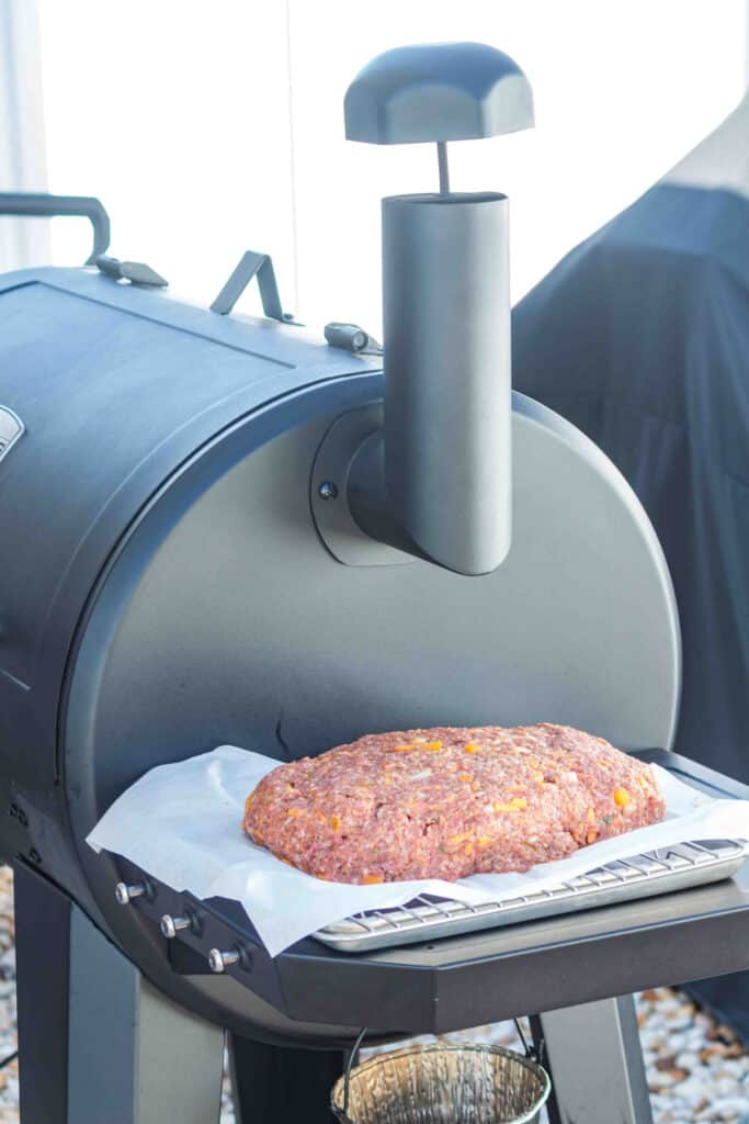 Shaped raw meatloaf on parchment paper next to the smoker.