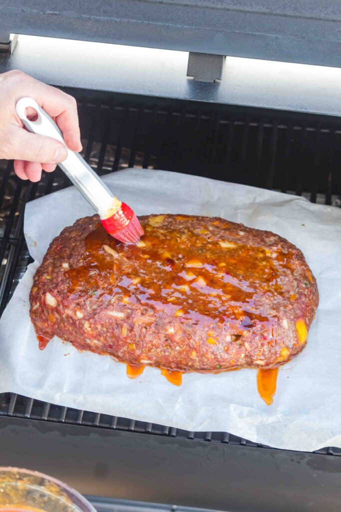 Peach bourbon BBQ sauce being brushed over the meatloaf inside the smoker