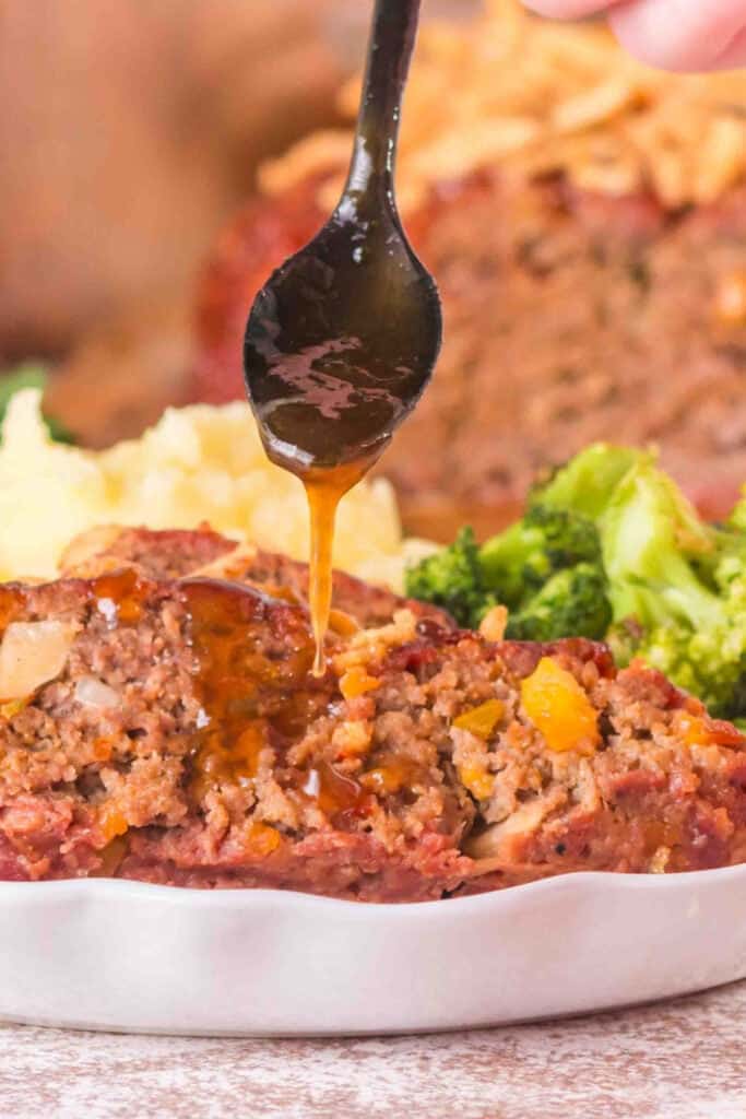 Peach bourbon BBQ sauce being spooned over sliced smoked cowboy meatloaf