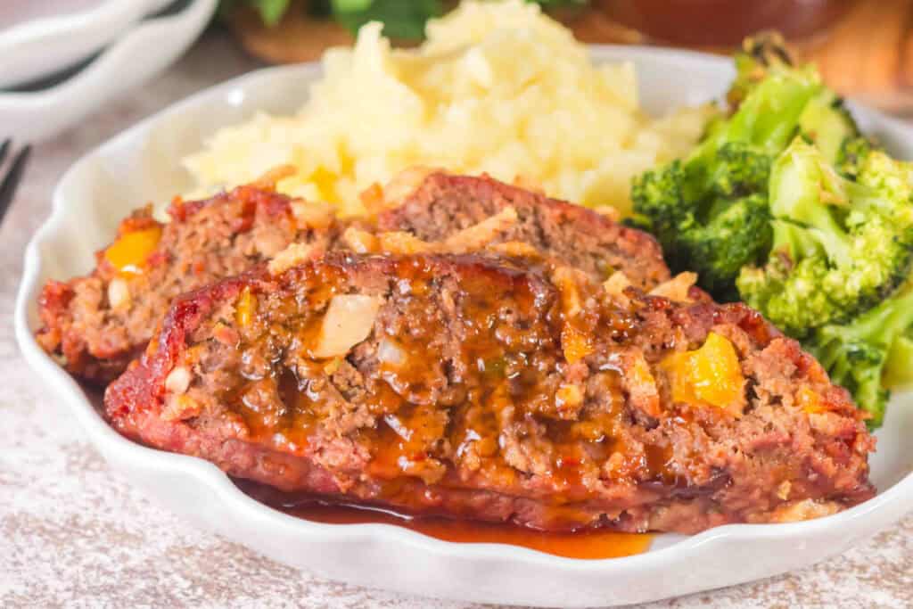Sliced Smoked Cowboy Meatloaf covered with sauce and served with mashed potatoes and broccoli