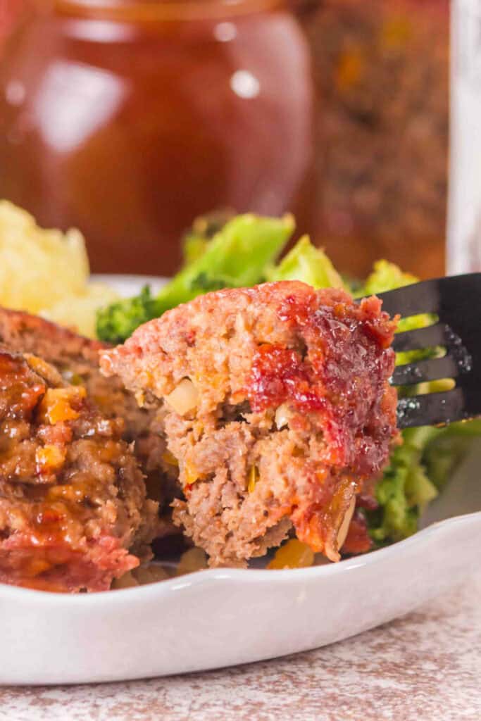 Fork holding a bite of glazed smoked cowboy meatloaf with visible peppers and onions
