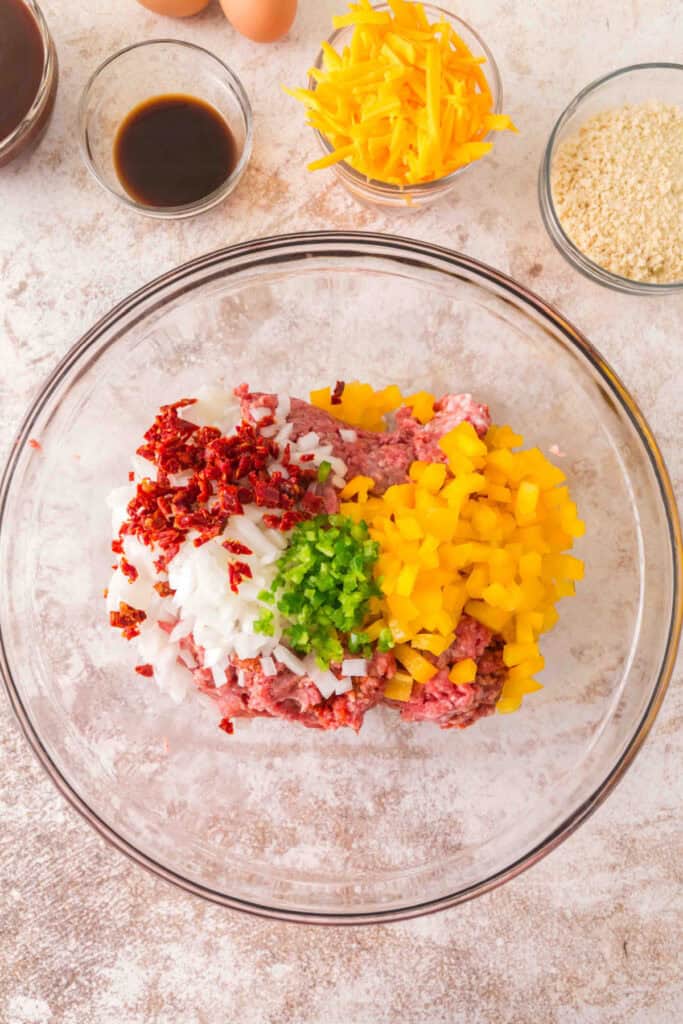 Ground meat mixture topped with seasonings, chopped onions, and peppers