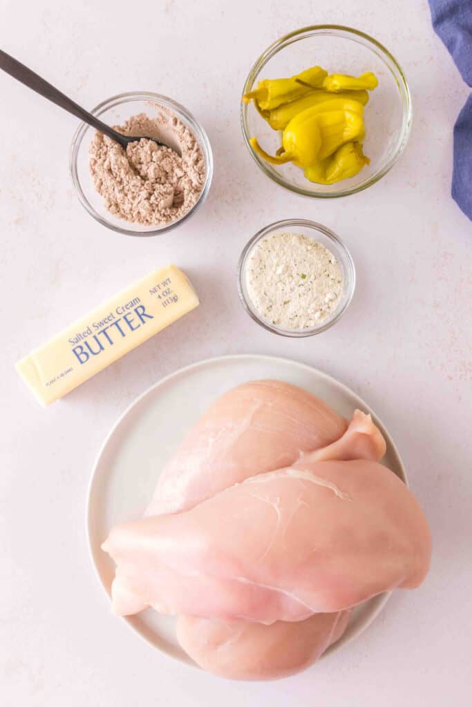 Ingredients for Mississippi chicken including chicken breasts, butter, pepperoncini, ranch seasoning, and au jus mix