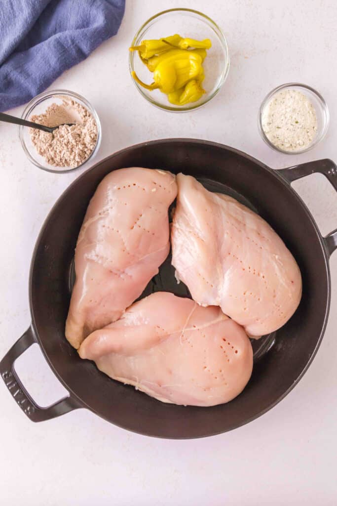 Raw boneless chicken breasts pierced with a fork in a cast iron skillet