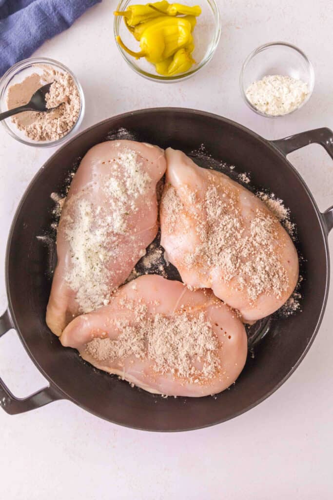Chicken breasts sprinkled with ranch seasoning and au jus gravy mix in a skillet