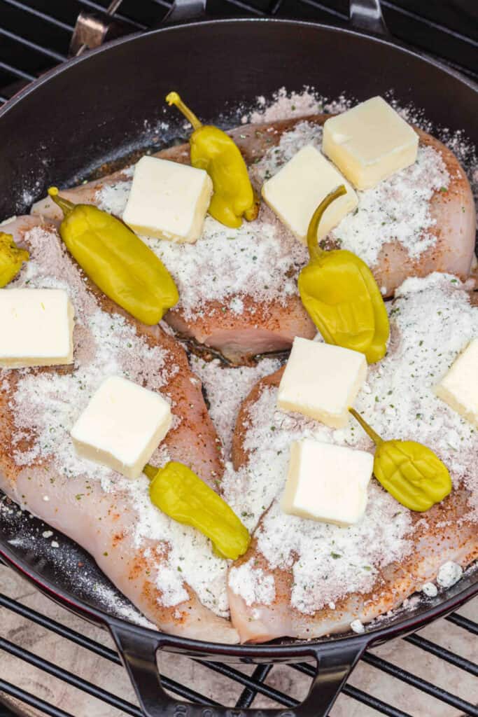 Close-up of chicken breasts topped with ranch, au jus, butter, and pepperoncini in the smoker