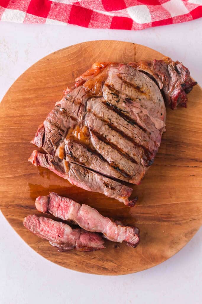 Reverse-seared ribeye steak partially sliced on a wooden cutting board to show the pink center.