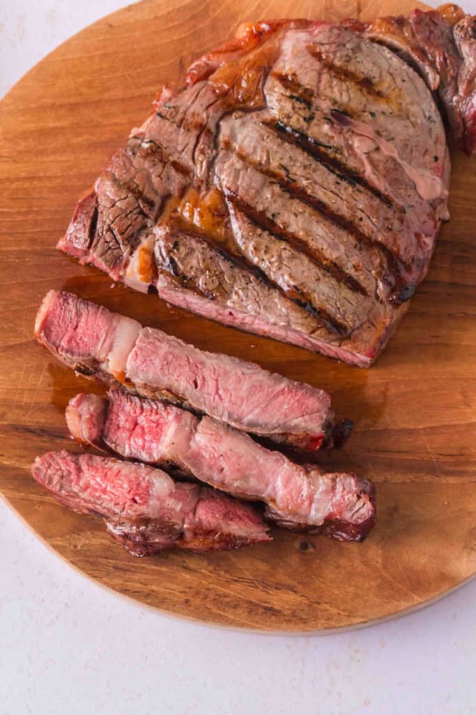 Smoked ribeye steak with grill marks and several thick slices arranged on a wooden cutting board.
