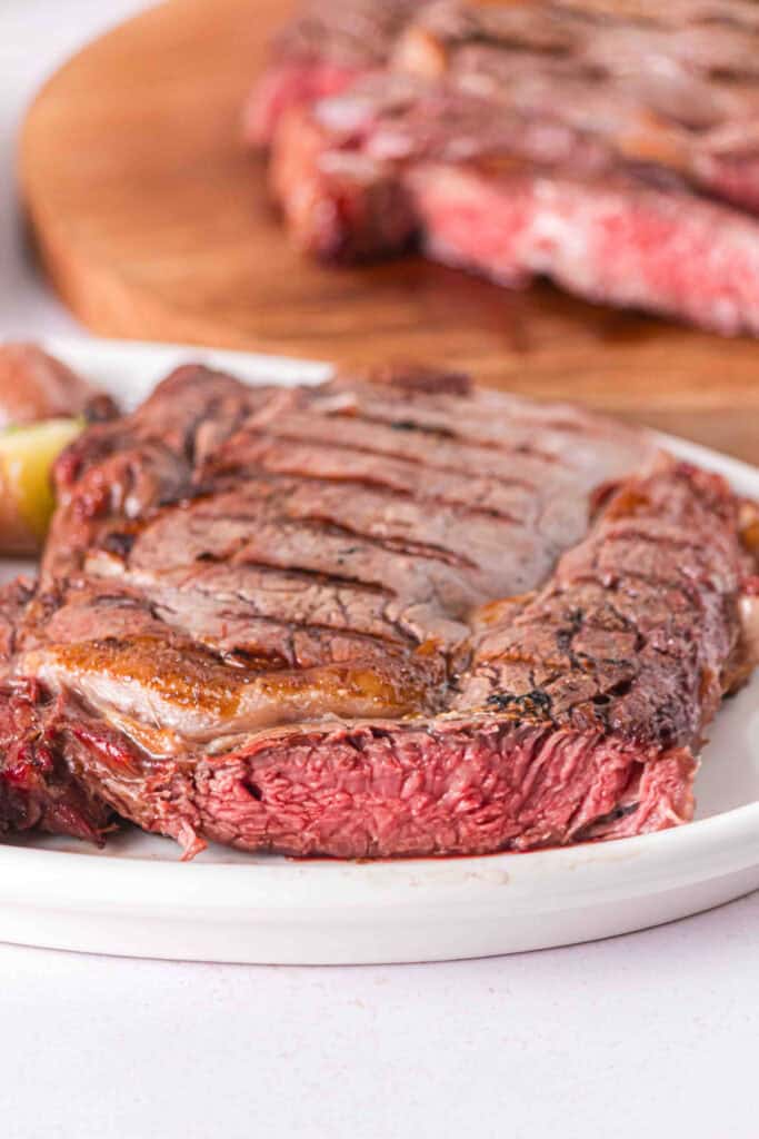 Smoked Ribeye with a seared exterior and juicy pink center served on a white plate.