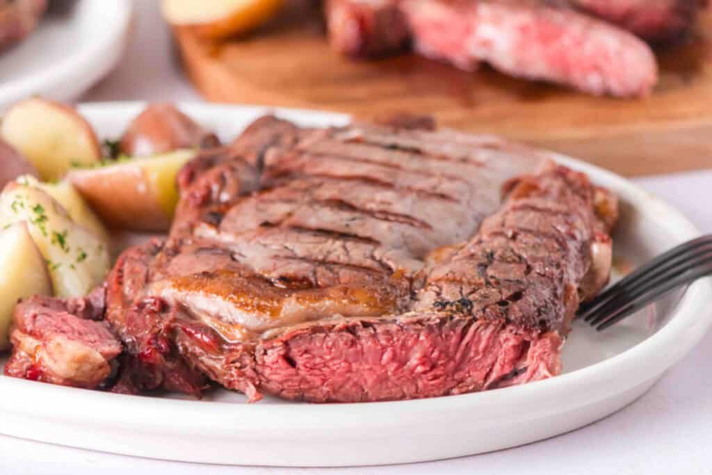 Grilled ribeye steak served with potatoes, showing the juicy pink interior and browned exterior.