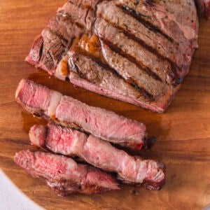 Sliced reverse-seared ribeye with grill marks and a pink center on a wooden cutting board.