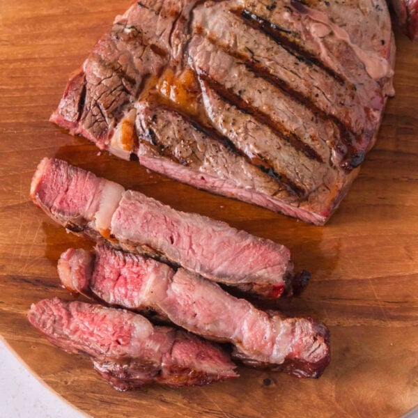 Sliced reverse-seared ribeye with grill marks and a pink center on a wooden cutting board.