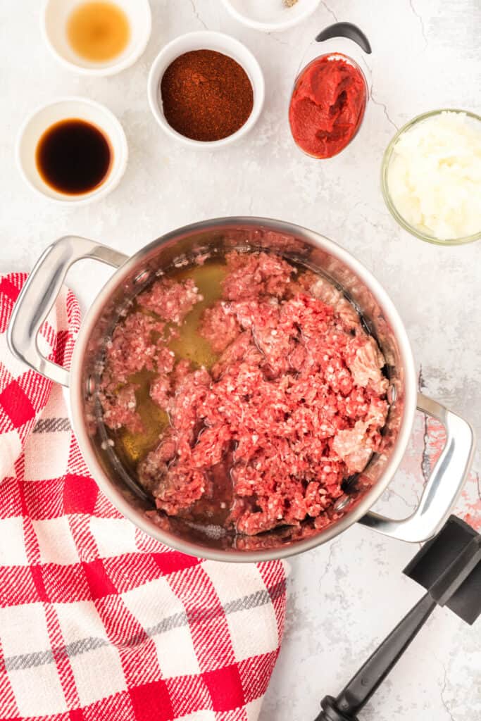 Ground beef cooking with beer and water in a saucepan before making homemade Southern Style Hot Dog Chili.