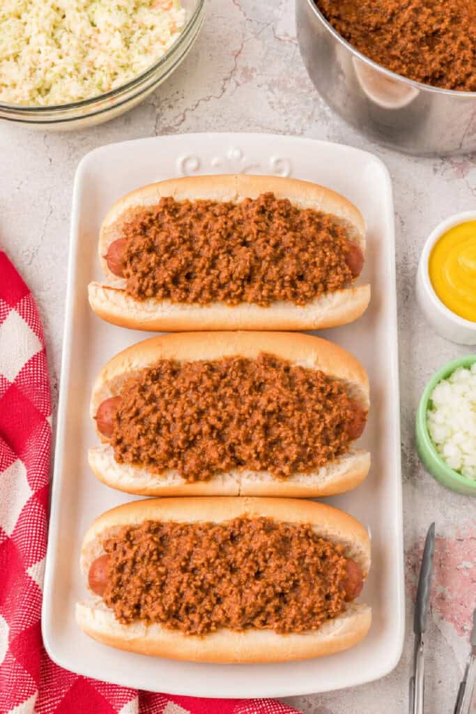 Three chili dogs topped with thick homemade Southern Style Hot Dog Chili served on a platter with classic toppings.