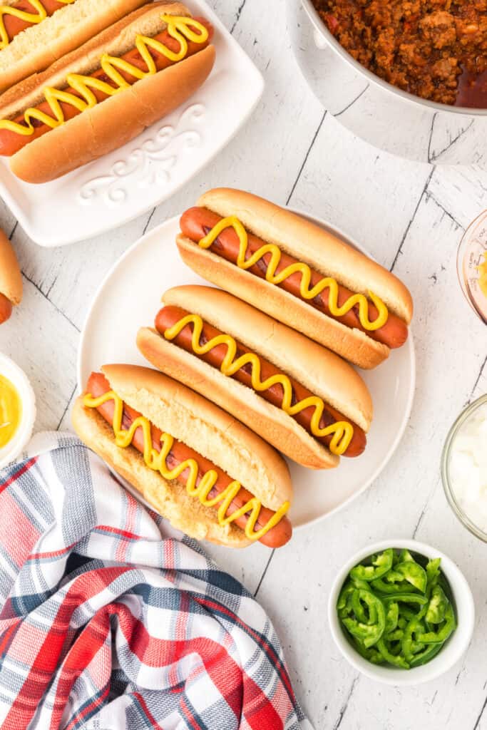 Hot dogs topped with yellow mustard before adding Texas chili and toppings