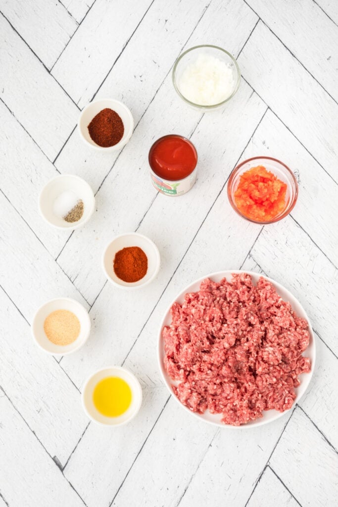 Ingredients for homemade Texas chili including ground beef, tomato sauce, onion, peppers, oil, and seasonings