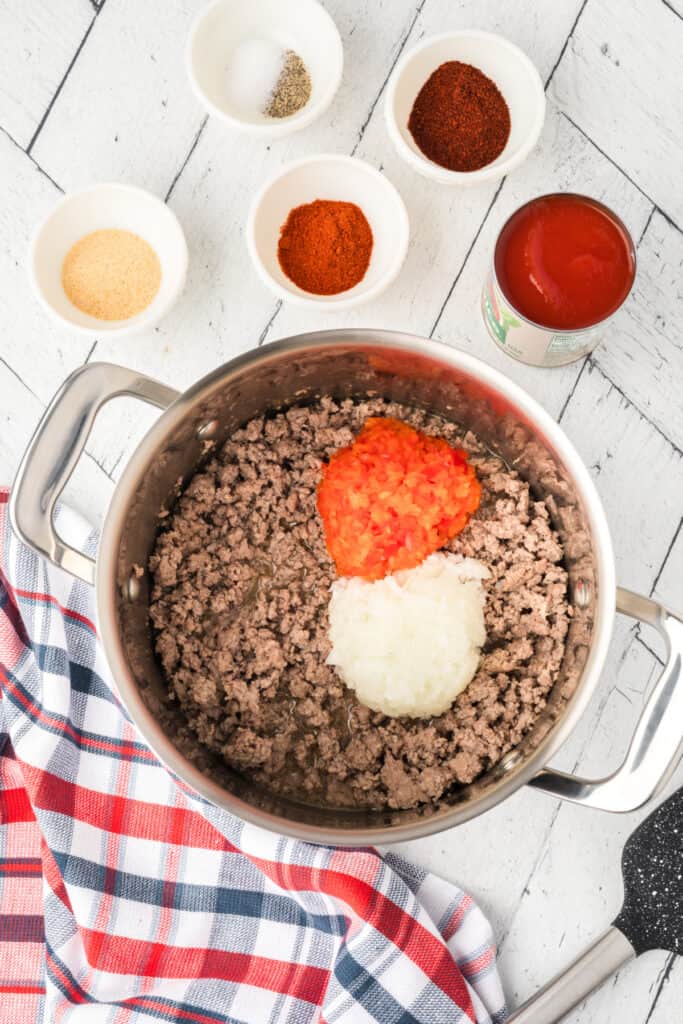 Chopped onion and peppers added to browned ground beef for Texas chili